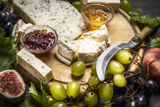 cheese plate with Gorgonzola and Camembert cheese knife honey jam light and dark grapes on a wooden cutting board close up