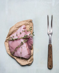 Fresh raw turkey breast with herbs and old meat fork on  blue wooden background, top view close up
