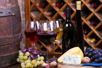 Red, rose and white glasses and bottles of wine. Grape, nuts, cheese and old wooden barrel