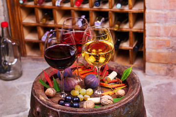 Red, rose and white glasses and bottles of wine. Grape, fig, nuts and leaves on old wooden barrel