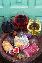 Red, rose and white  glasses and bottles of wine. Cheese, fig, grape, prosciutto and bread on old wooden barrel