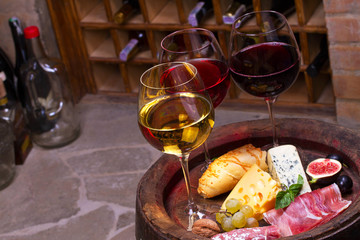 Red, rose and white  glasses and bottles of wine. Cheese, fig, grape, prosciutto and bread on old wooden barrel