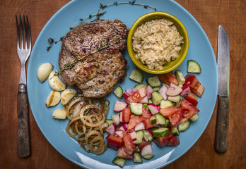 succulent roast pork garlic and onion sauce salad with garlic fried onions and herbs on a blue plate with fork and knife on wooden background top view close up