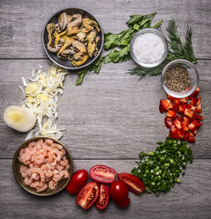 shrimp and mussels in metal bowls with spices onion pepper tomatoes and herbs lined circle frame on wooden background top view