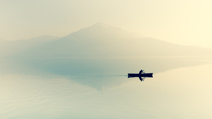 Fototapeta na wymiar Fog over the lake. Silhouette of mountains in the background. The man floats in a boat with a paddle. Filter soft light.