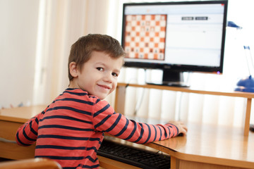 Fototapeta na wymiar Little boy playing on PC chess looking back