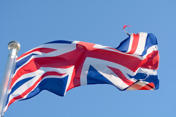 The Union Jack flag fluttering wildly in the wind on a sunny day