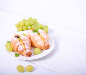 Fresh croissant with grapes on white background