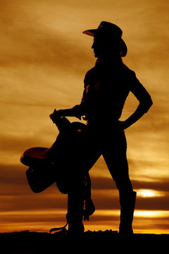 silhouette of a cowgirl holding saddle on hip