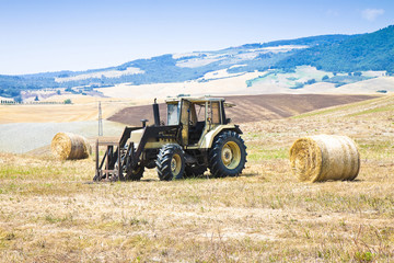 Old tractor stopped in a hill with round bales on background