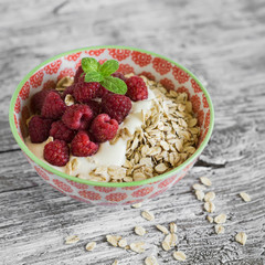 oatmeal with raspberries, strawberries and natural yoghurt in a bowl on a light wooden background