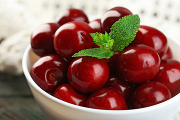 Sweet cherries with green leaves in bowl, on wooden background