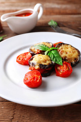 Dish of eggplant with cherry tomatoes and cheese in white plate on wooden table, closeup