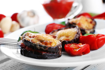 Dish of eggplant with cherry tomatoes and cheese in white plate on wooden table, closeup