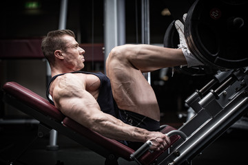 Fototapeta na wymiar Man in gym training at leg press