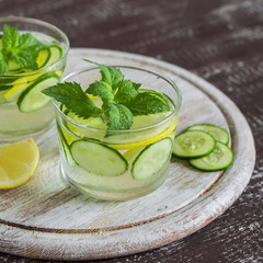 Lemonade with cucumber, lemon, mint and ginger in glass cups on a wooden surface