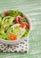 fresh salad with avocado, tomato and mozzarella, in a white bowl on bright wooden surface