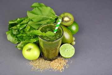 Green healthy juice with fruits and herbs on gray background