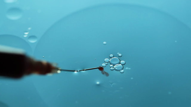 Abstract close-up of floating oil drops and syringe and blood on water surface