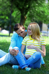 Young pregnant woman with husband sitting on green grass in park