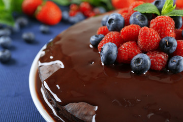 Delicious chocolate cake with summer berries on blue tablecloth, closeup