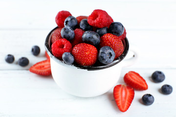 Tasty ripe berries in cup on wooden table close up