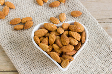 Almonds in heart-shaped bowl on a sack.