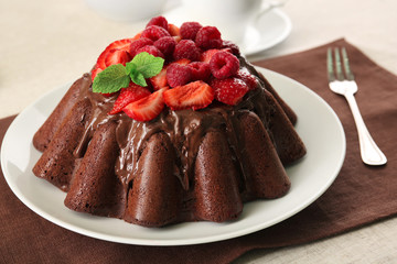 Tasty chocolate muffin with glaze and berries on table close up