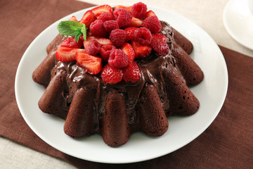 Tasty chocolate muffin with glaze and berries on table close up
