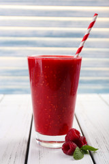 Raspberry cocktail and raspberries on wooden surface on light background