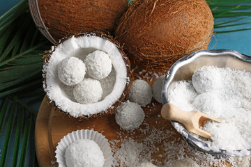 Candies in coconut flakes and fresh coconut on color wooden background