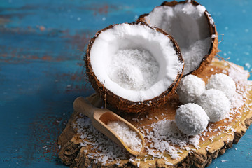 Candies in coconut flakes and fresh coconut on color wooden background