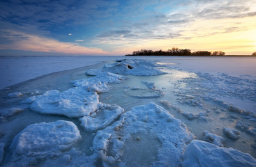 Winter landscape with frozen lake and sunset sky. 