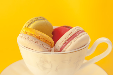Pile of colorful macarons stacked up in the white classic cup in yellow pastel isolated background