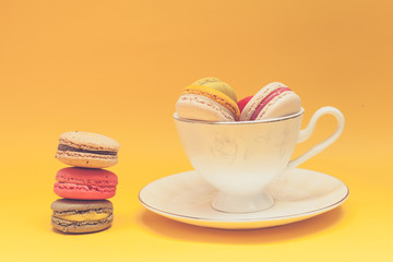 Pile of colorful macarons stacked up in the white classic cup in yellow pastel isolated background