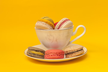 Pile of colorful macarons stacked up in the white classic cup in yellow pastel isolated background