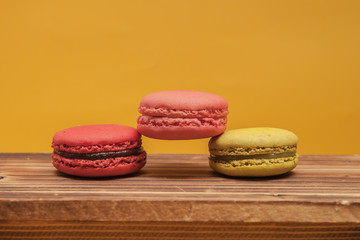 Obraz na płótnie Canvas Pile of colorful macarons stacked up in yellow pastel isolated background on wood table