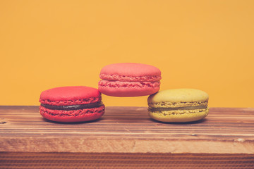 Pile of colorful macarons stacked up in yellow pastel isolated background on wood table