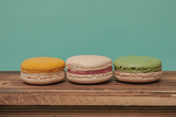 Set of colorful macarons sitting next to each other in blue turquoise pastel isolated background on wood table