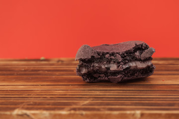 Purple color of bitten macaron on the wood table in red pastel isolated background