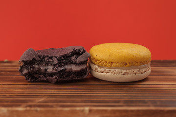 Set of macarons in various colors on wood table in red pastel isolated background. Some of them are bitten.