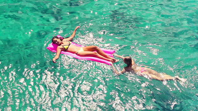 Beautiful Young Women In Bikinis Floating on Pink Inflatable Raft in Crystal Ocean in Hawaii. Summer Fun Vacation Lifestyle. Diverse Ethnic Pacific Islander Hawaiian Girl with Blonde Girl Friend. 