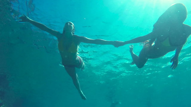 Beautiful Girls in Bikinis Swimming Underwater Holding Hands in Pacific Ocean. Hawaiian Ethnic Girl with Young Blonde Girl Friend. Summer Fun Lifestyle.