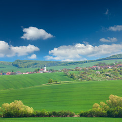 Fototapeta na wymiar Little town on the green hills, blue sky, beautiful buildings