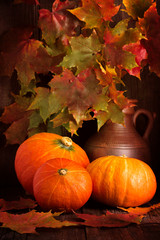 Naklejka na ściany i meble Autumn pumpkin with maple leaves on wooden background.
