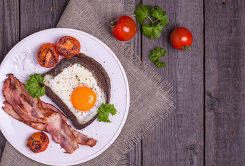 Fried eggs in rye bread with bacon, tomatoes and parsley in rust