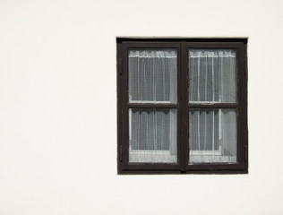 Old black wooden window with curtain on a white facade.