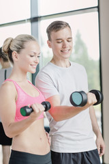 smiling young woman with personal trainer in gym