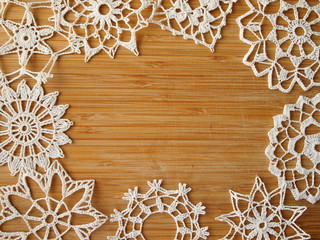 Frame for a text formed by crocheted snow flakes on a wooden background.