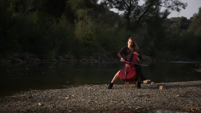Beautiful girl is  playing the cello at the river